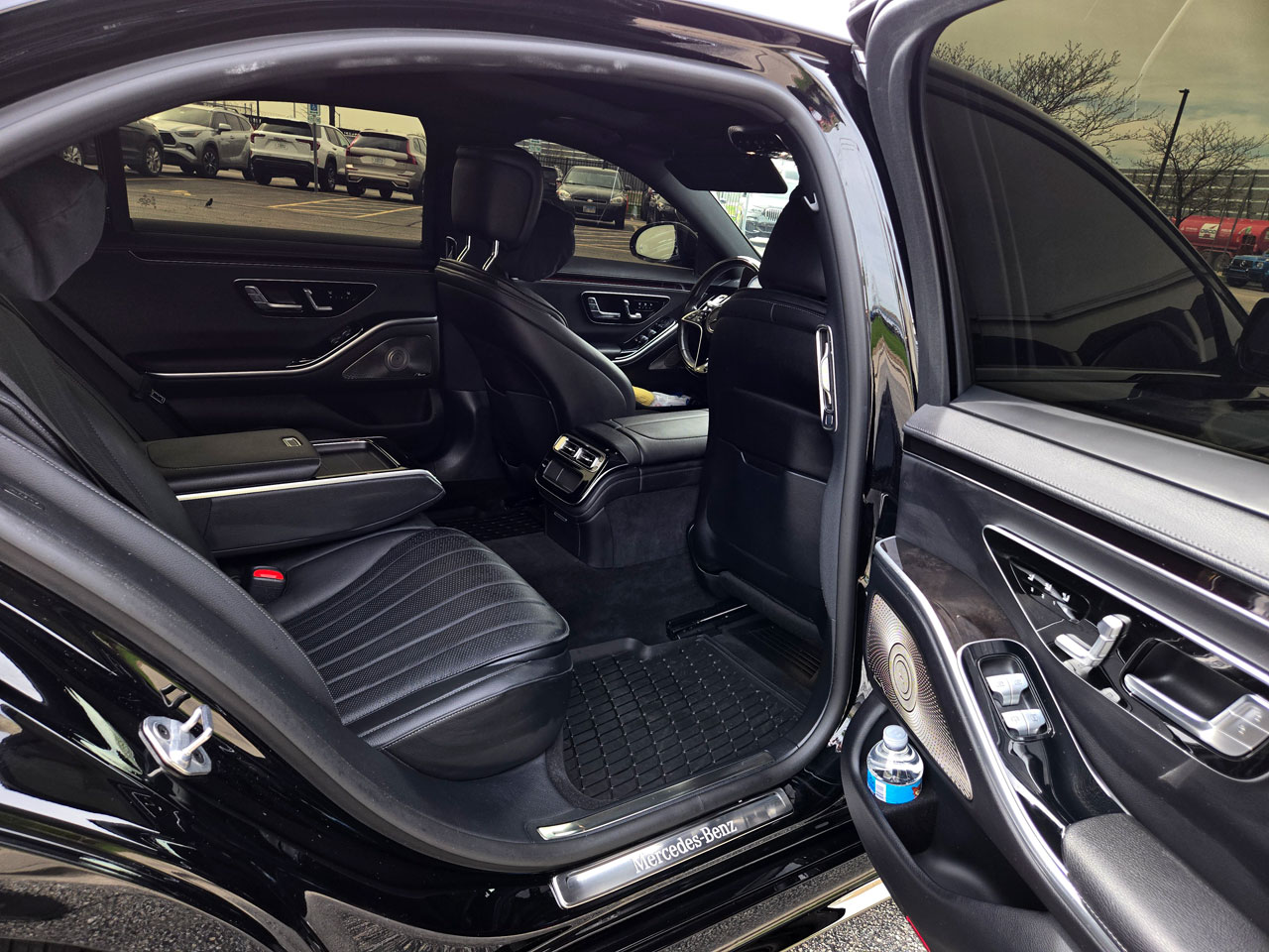 Open rear door of a black Mercedes-Benz, revealing the luxurious black leather rear seats, center console, and a water bottle in the door pocket.