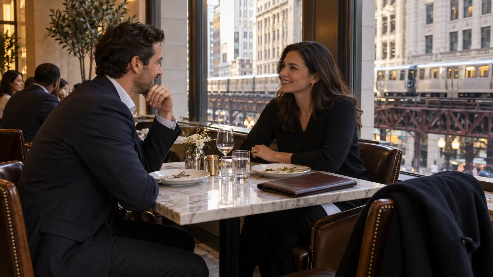 Two colleagues finishing a meal beside a Chicago window with a closed work folio