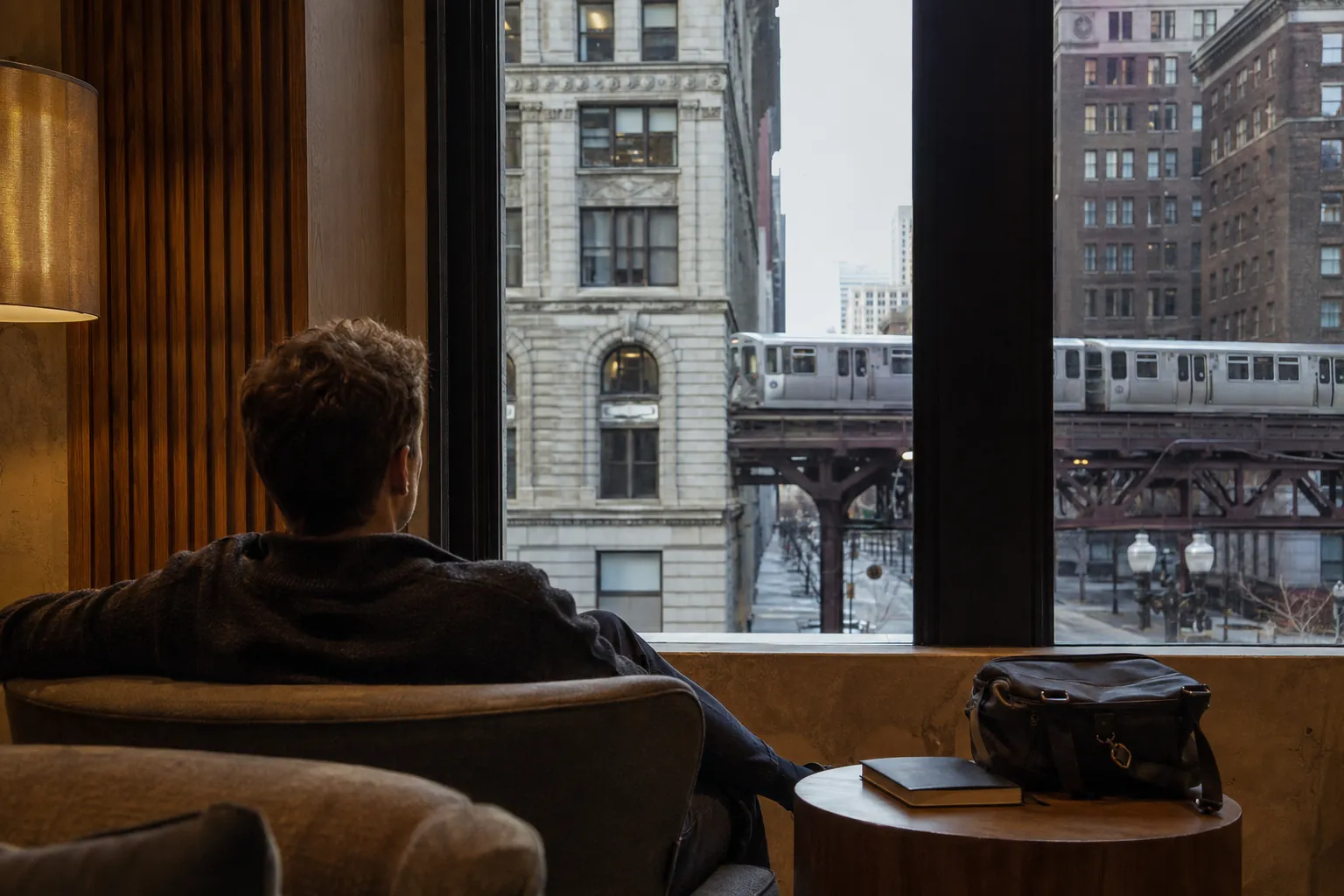 A hotel guest resting beside a window overlooking Chicago elevated tracks