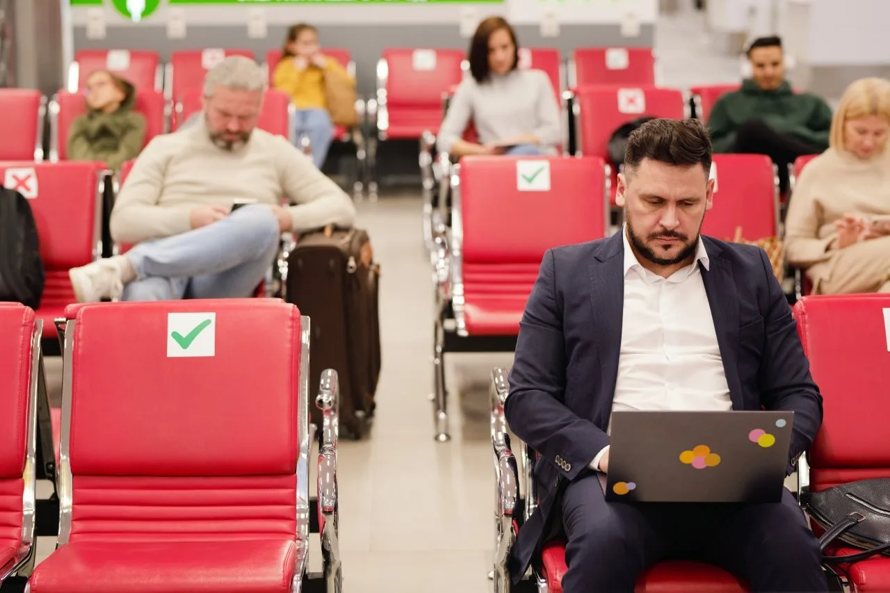 A man in a dark suit using a laptop in red airport seating