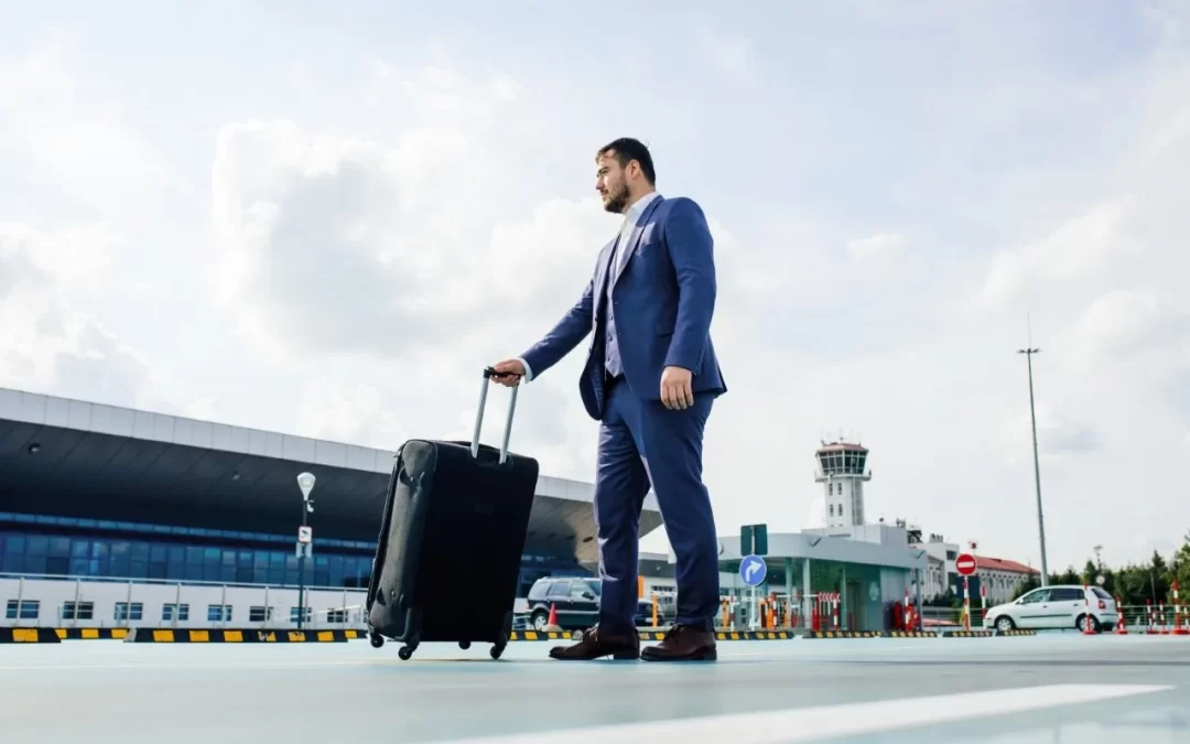 A man in a blue suit pulling a black suitcase outside an airport terminal