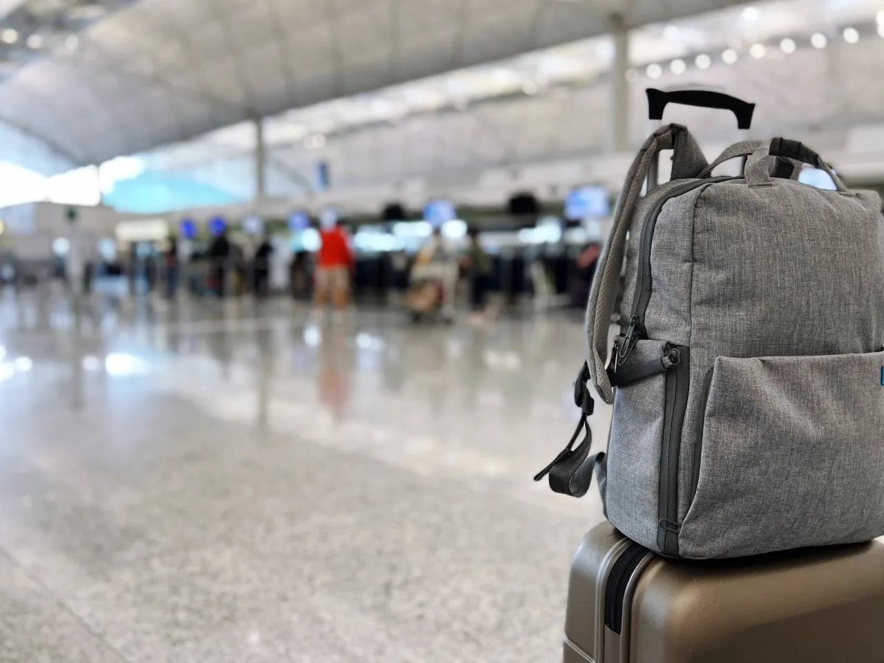 A gray backpack resting on a wheeled suitcase inside an airport terminal