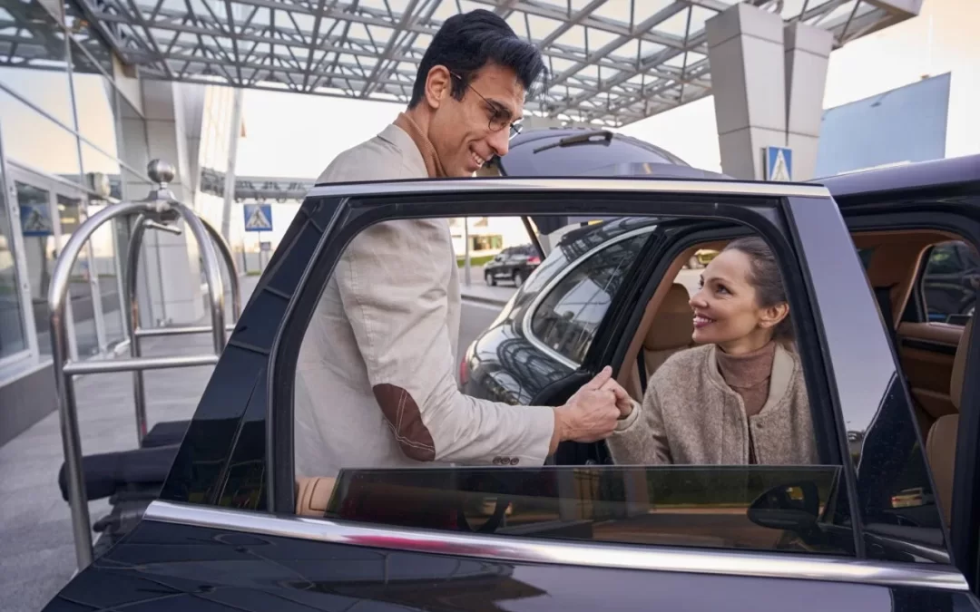 A man assisting a woman seated in a dark car outside a building entrance