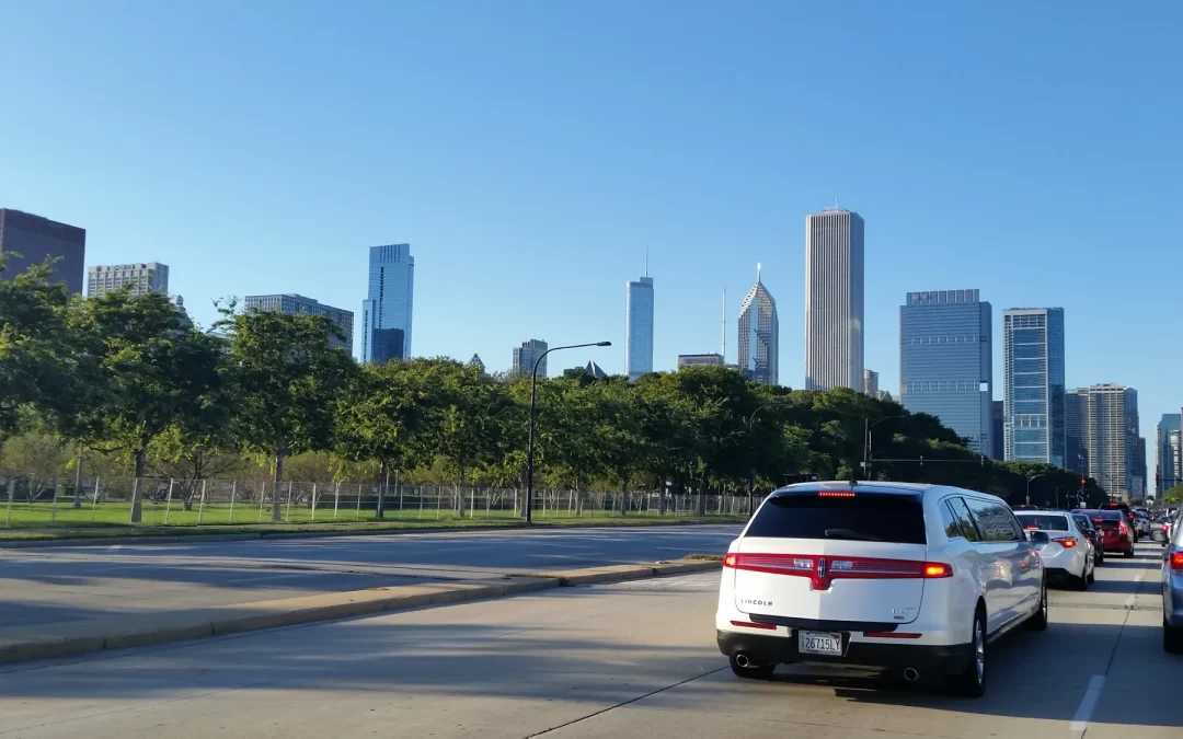A white limousine in street traffic with the Chicago skyline beyond trees
